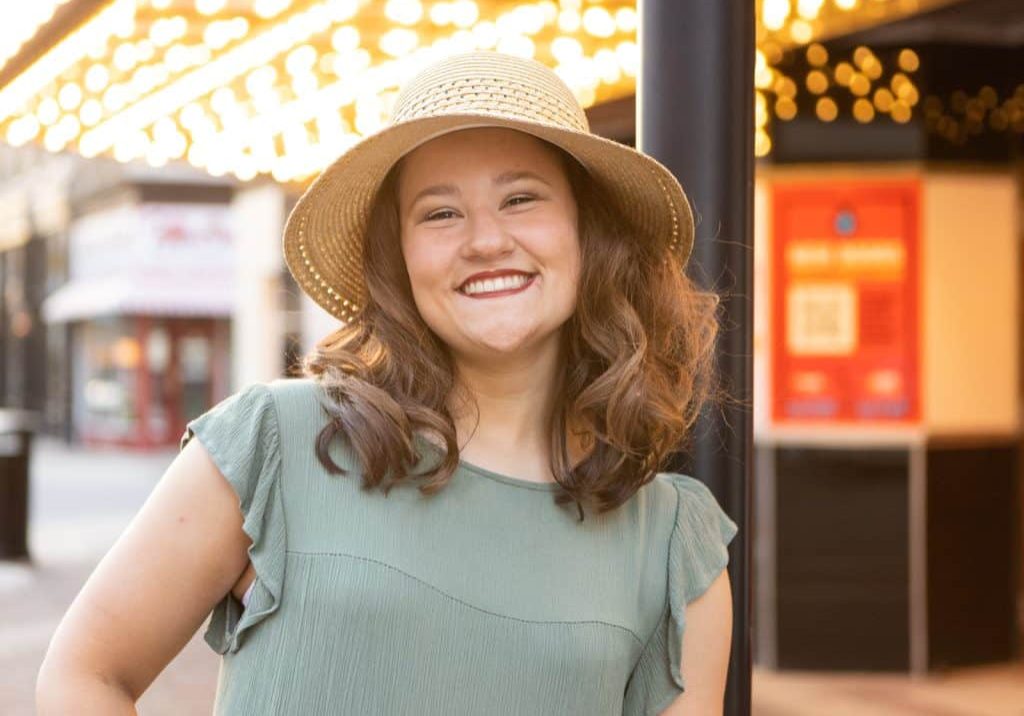 Senior photo session for a senior girl as she poses in front of theater lights in a hat and green dress