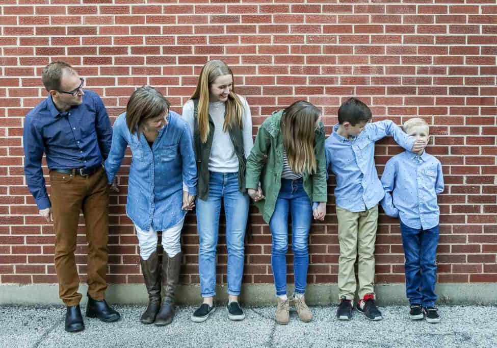 Family of 6 poses along a brick wall downtown for a photo
